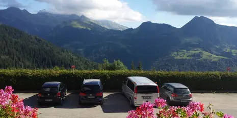 Photo of the view from the accommodation. Behind the parking lot in the foreground, the green mountains stand mightily.